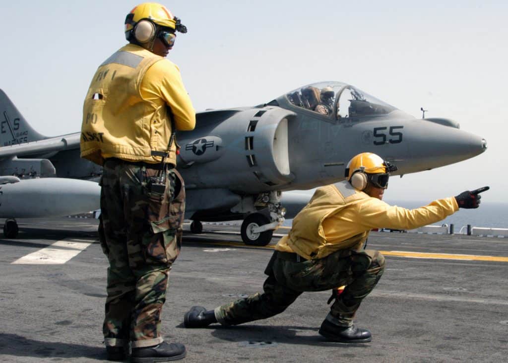 Two Navy men on Air Craft Carrier directing jet for take off.