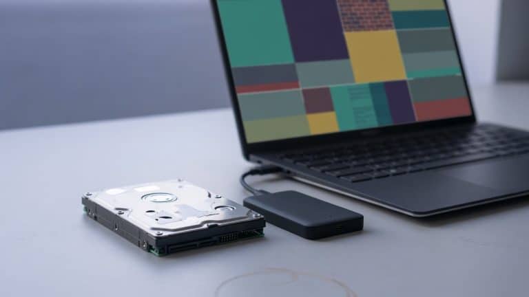 Desktop and portable hard drives beside a laptop whose screen shows an abstract disk partition map